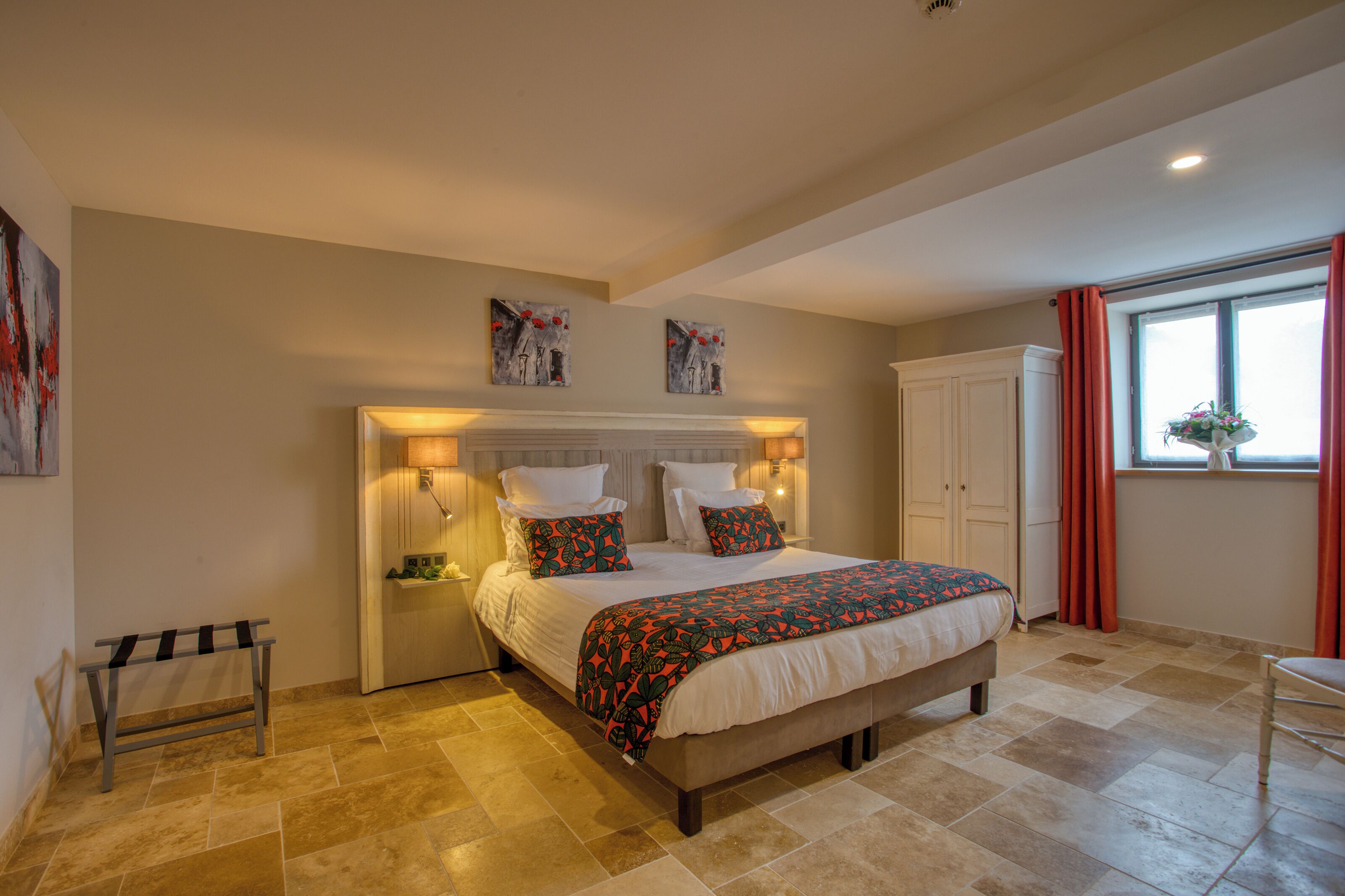 A bedroom with a large bed, bedside lamps, a nightstand, a bench, and artwork on the walls.