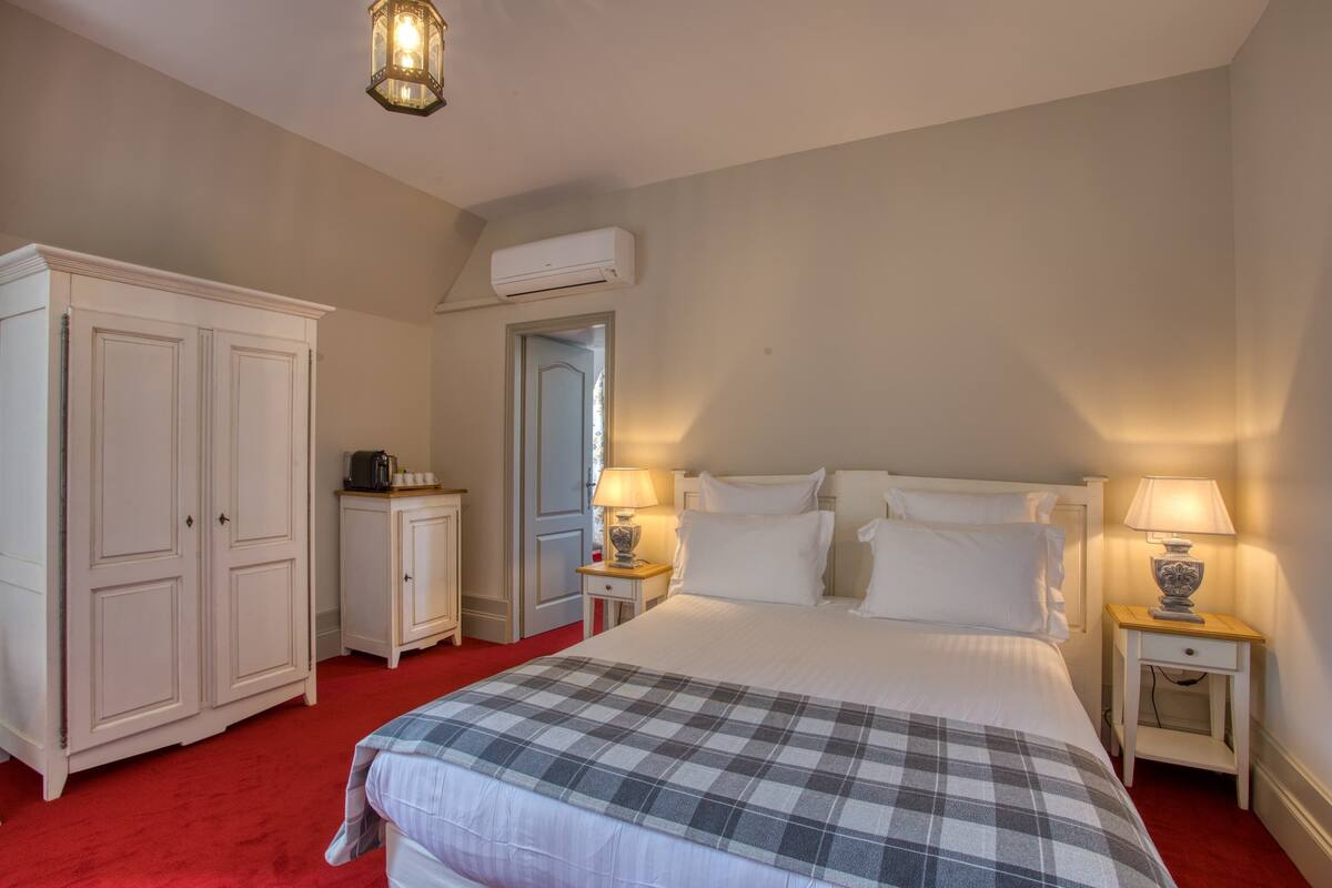 A bedroom with a large bed, two bedside tables with lamps, a wardrobe, and an air conditioning unit.
