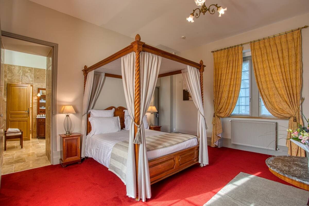 A four-poster canopy bed with a red carpet, wooden furniture, and a chandelier.