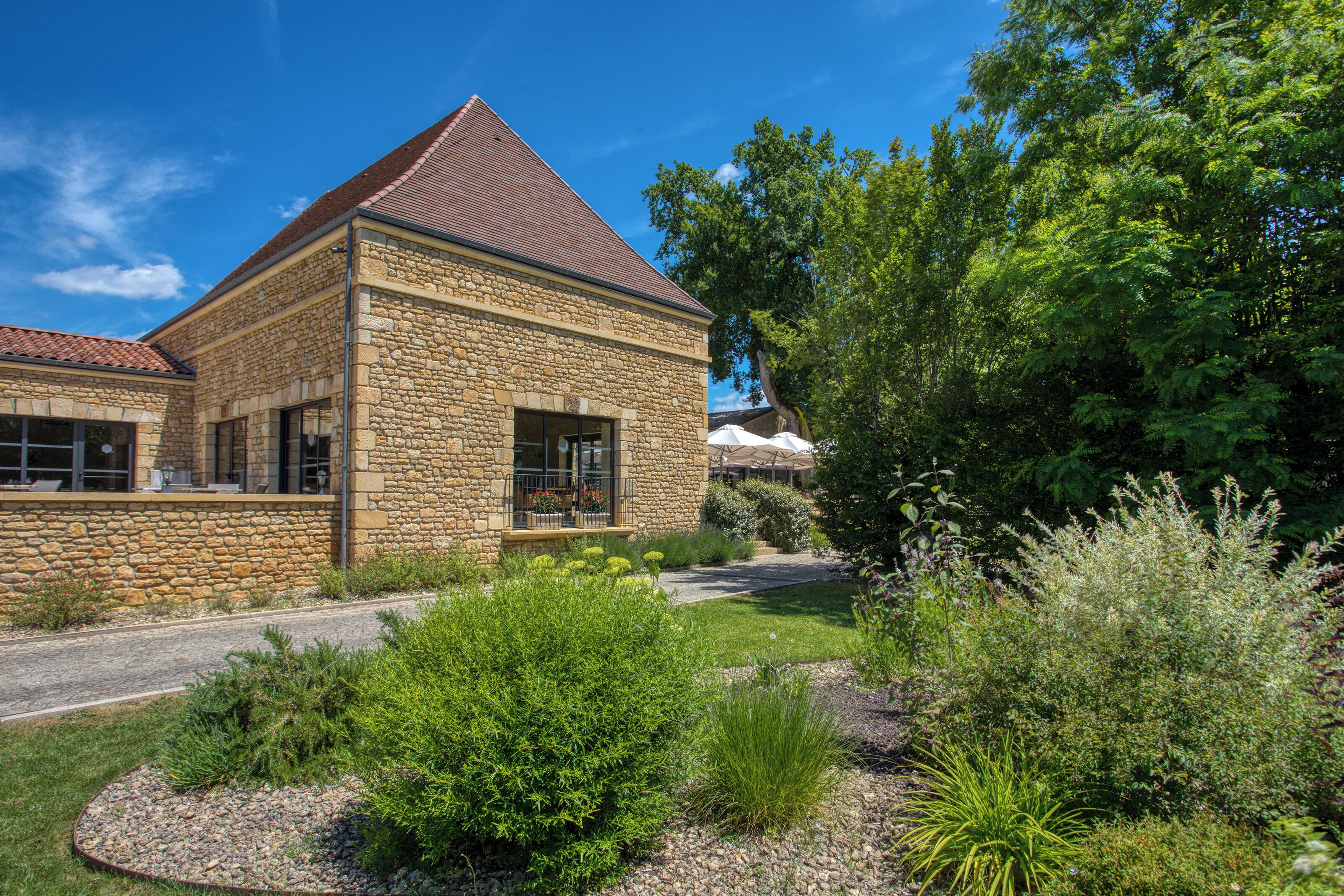 A stone building with a sloped roof, surrounded by a well-maintained garden with various plants and a gravel path.