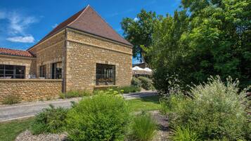 A stone building with a sloped roof, surrounded by a well-maintained garden with various plants and a gravel path.