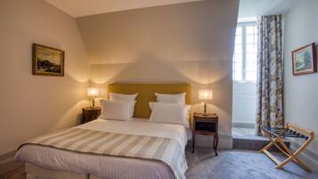 Une chambre à coucher avec un lit, deux tables de chevet avec des lampes, une fenêtre avec des rideaux et un tableau au mur.