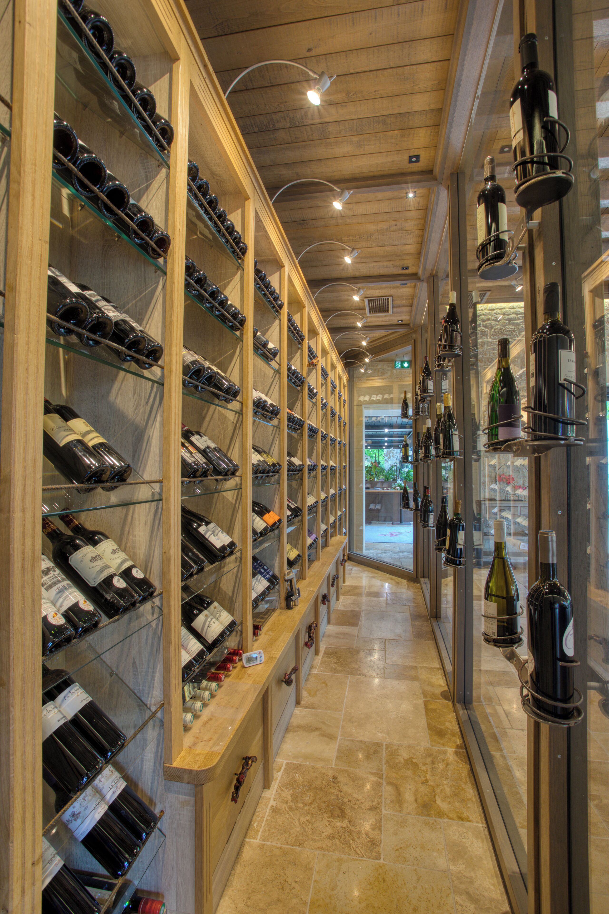 A wine cellar with shelves of wine bottles, a wooden counter, and a view into the restaurant area.