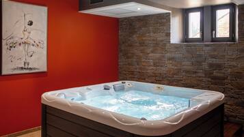 A hot tub in a room with red walls, a stone wall, and a window.
