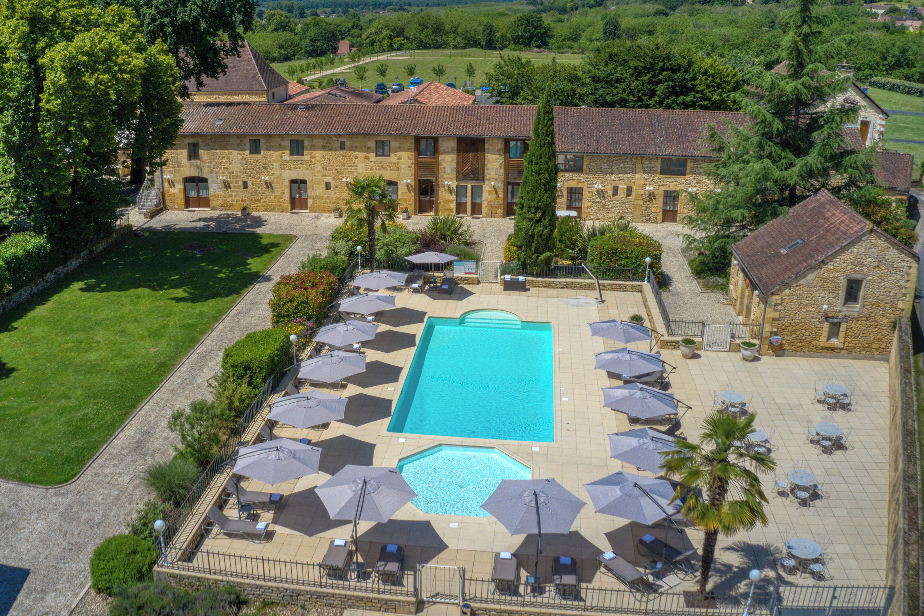 A large stone building with a swimming pool surrounded by umbrellas and lounge chairs.