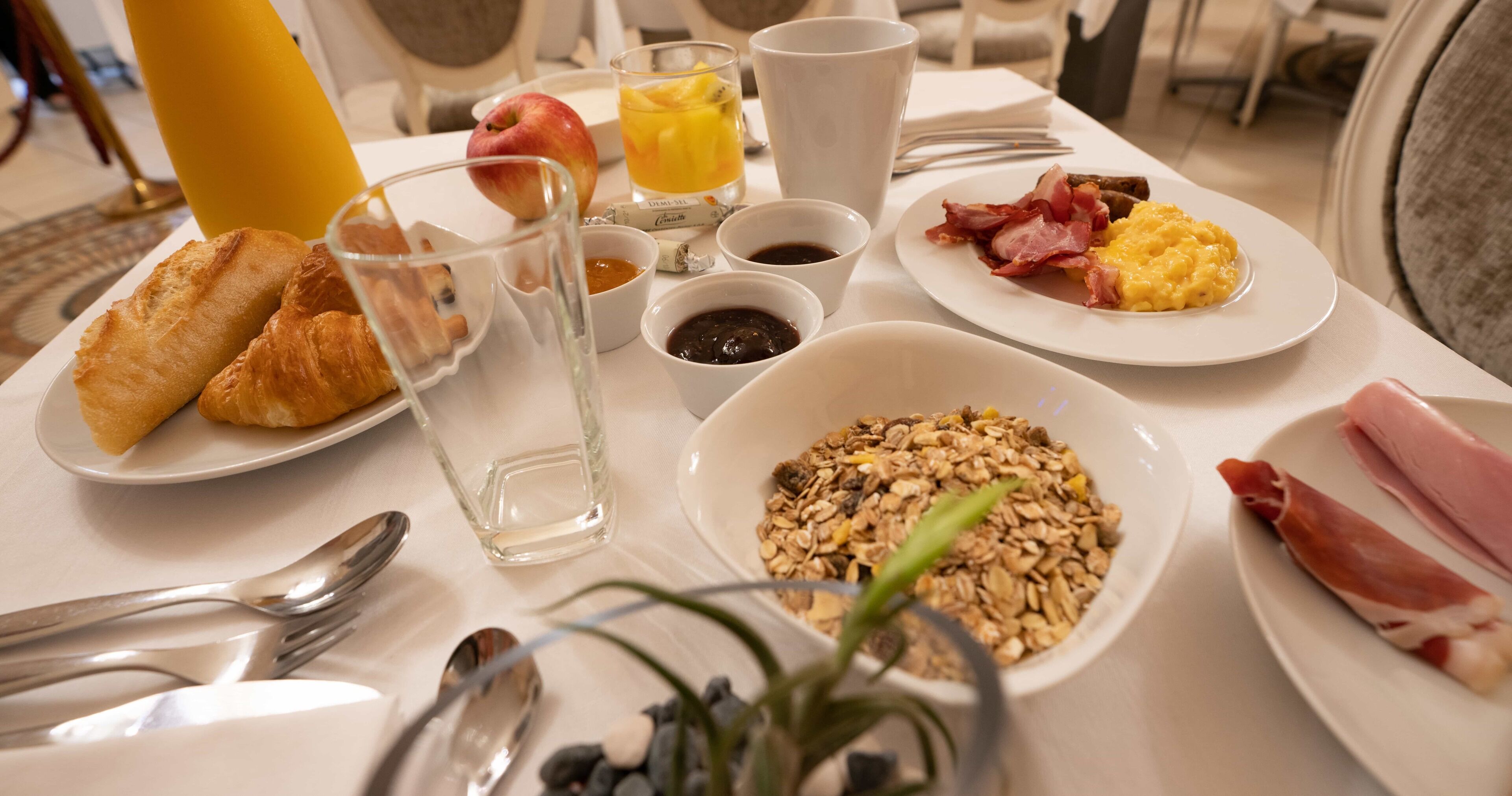 Ein Frühstückstisch mit Croissants, Rührei, Speck und einer Schüssel Granola.