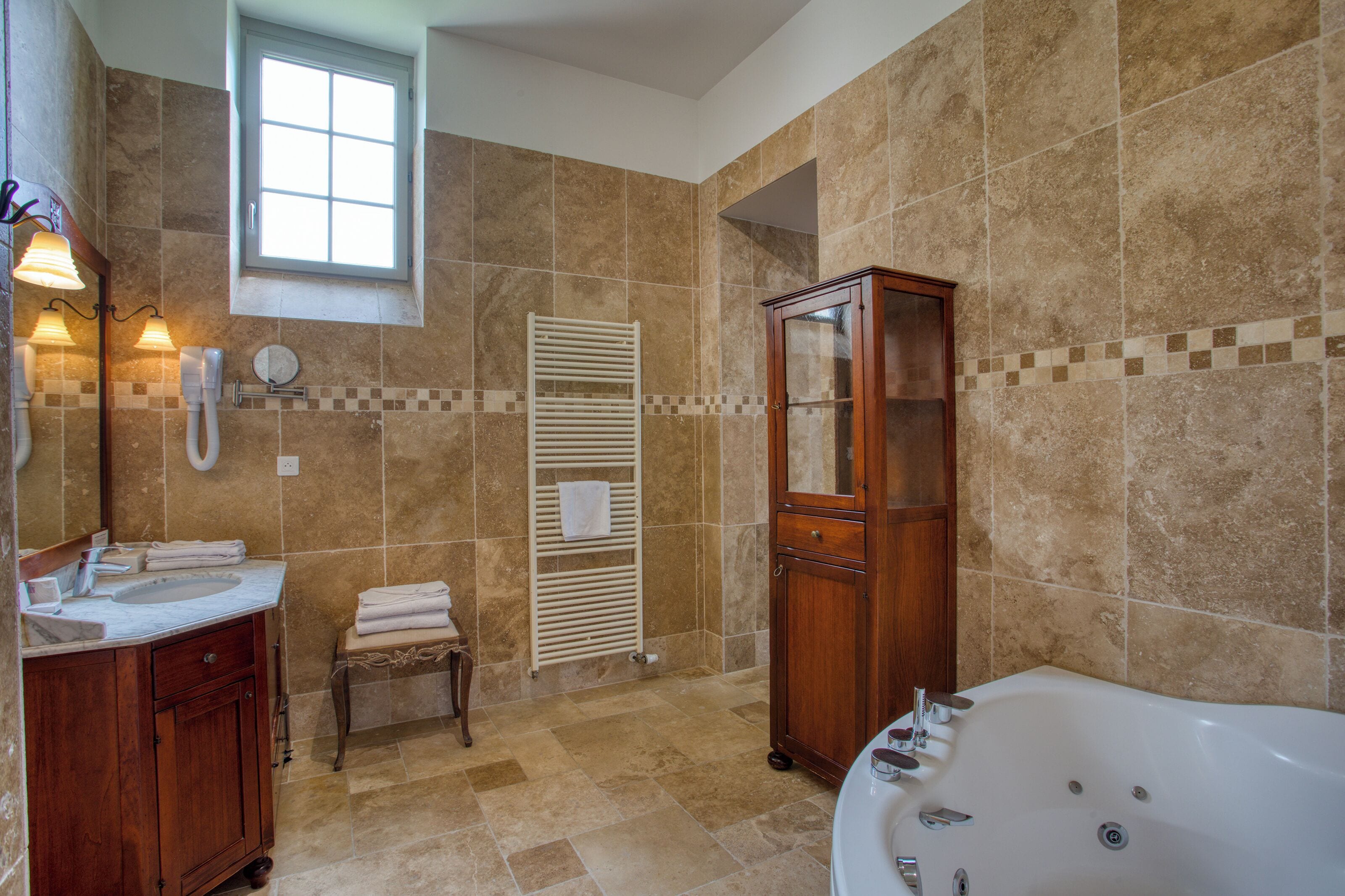 A bathroom with a bathtub, a wooden cabinet, a vanity with a mirror, and a towel rack.