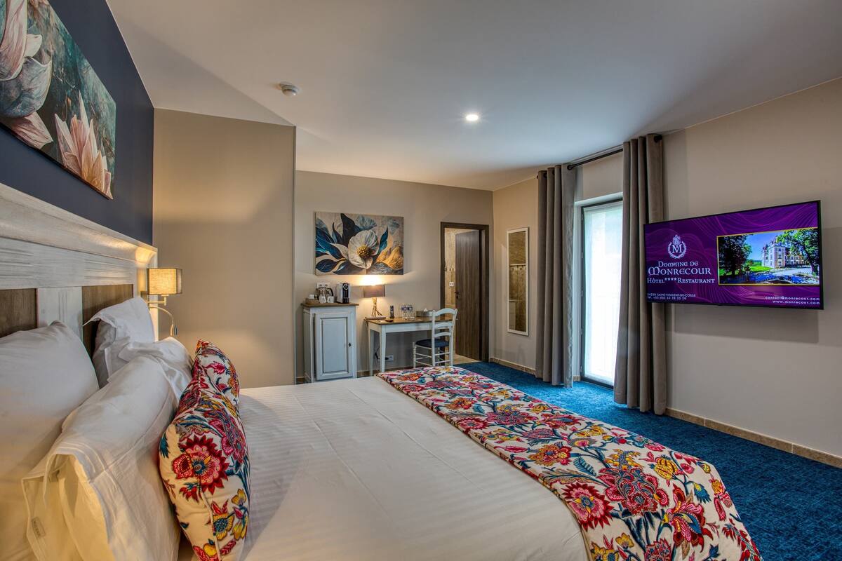 A hotel room with a large bed, a desk, a chair, a television, and a painting on the wall.