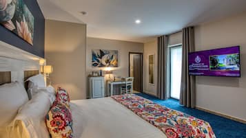 Una habitación de hotel con una cama grande, un escritorio, una silla, un televisor y un cuadro en la pared.