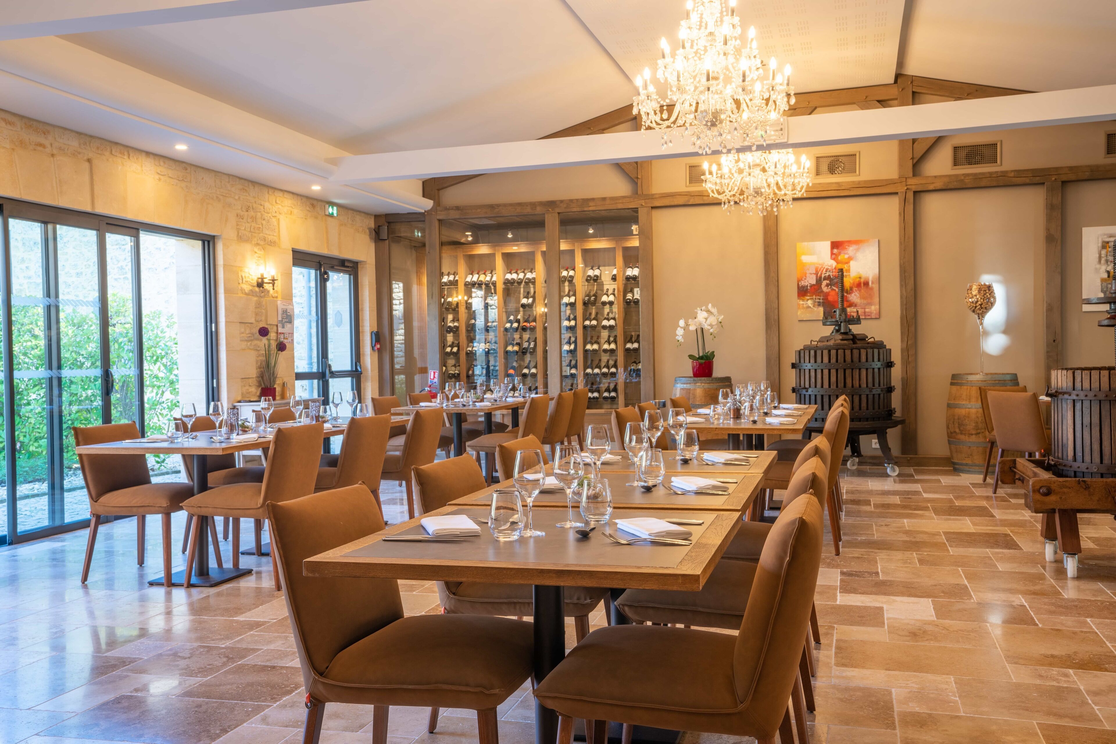 Un restaurante espacioso con techos altos, candelabros y una cava de vinos visible a través de las puertas de cristal.