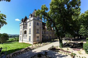 A large, historic stone building with multiple stories and a prominent tower, surrounded by well-maintained gardens and a clear blue sky. - Domaine du Château de Monrecour – Hôtel et Restaurant (Saint-Vincent-de-Cosse)