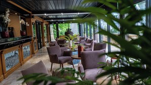 A modern interior with a bar area, seating, and large windows offering a view of greenery. - Domaine du Château de Monrecour – Hôtel et Restaurant (Saint-Vincent-de-Cosse)