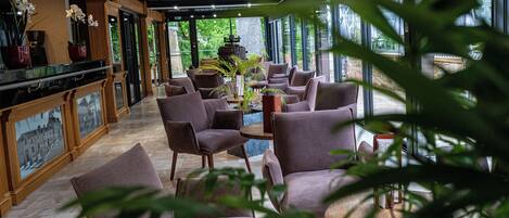 A modern interior with a bar area, seating, and large windows offering a view of greenery.