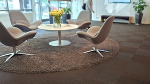 Un vestíbulo moderno con una mesa redonda, cuatro sillas, un jarrón con flores y una pantalla grande al fondo.