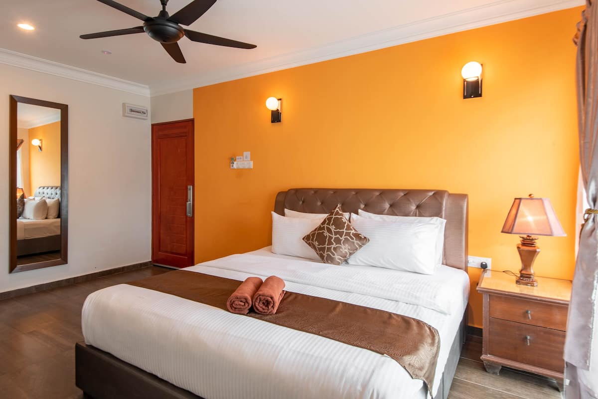 A hotel room with a large bed, a ceiling fan, a nightstand with a lamp, and a wooden door.