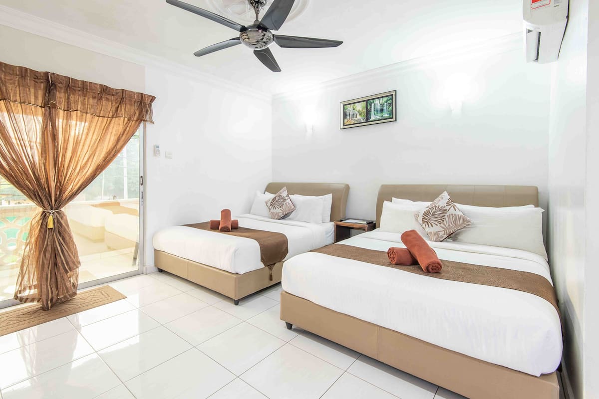 A hotel room with two beds, a ceiling fan, a large window with curtains, and a picture on the wall.