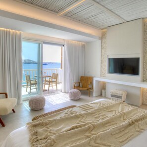 A hotel room with a large bed, a TV, a balcony with a view, and a seating area.