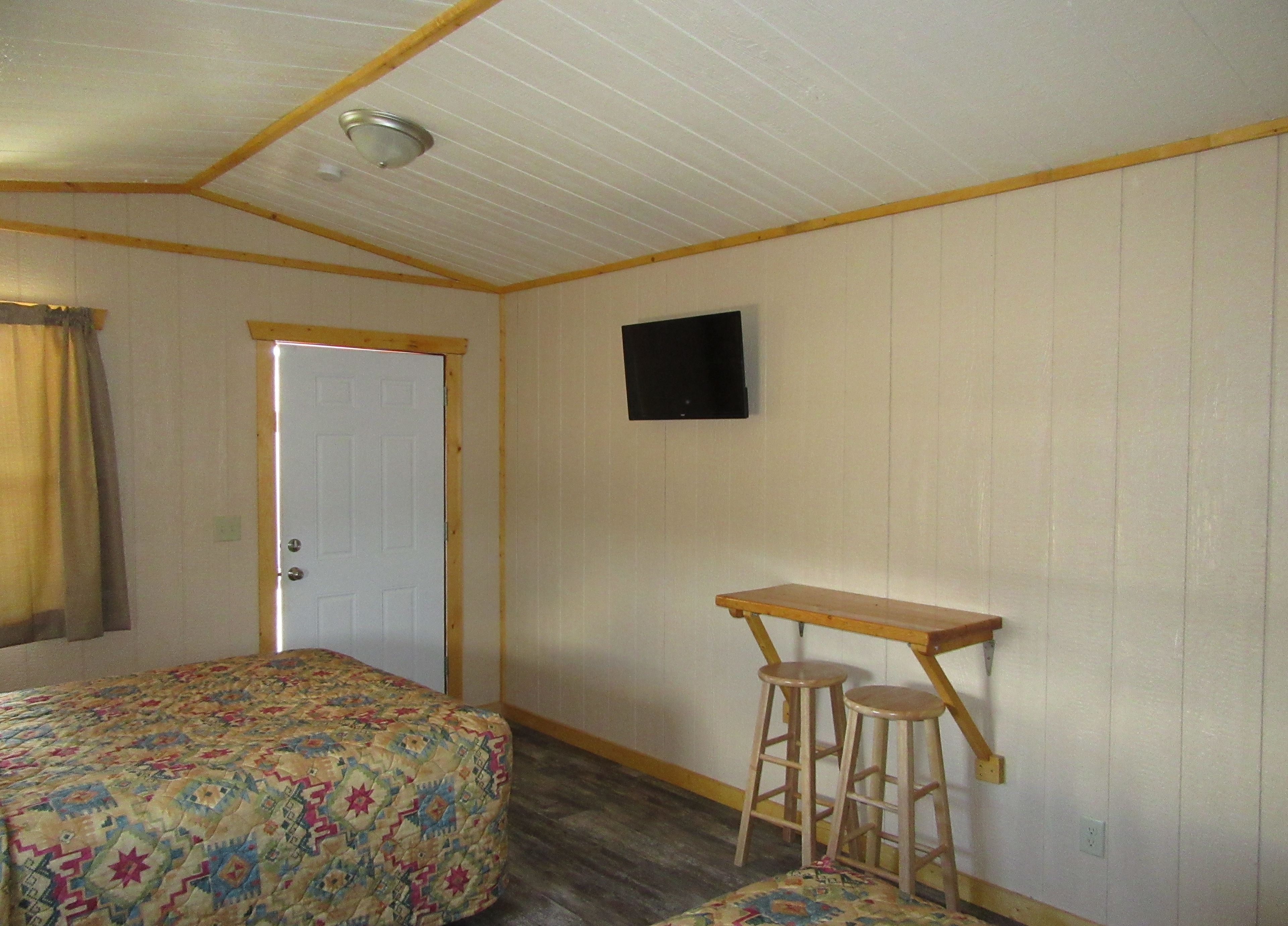 A room with two beds, a small table with stools, a door, and a mounted television.