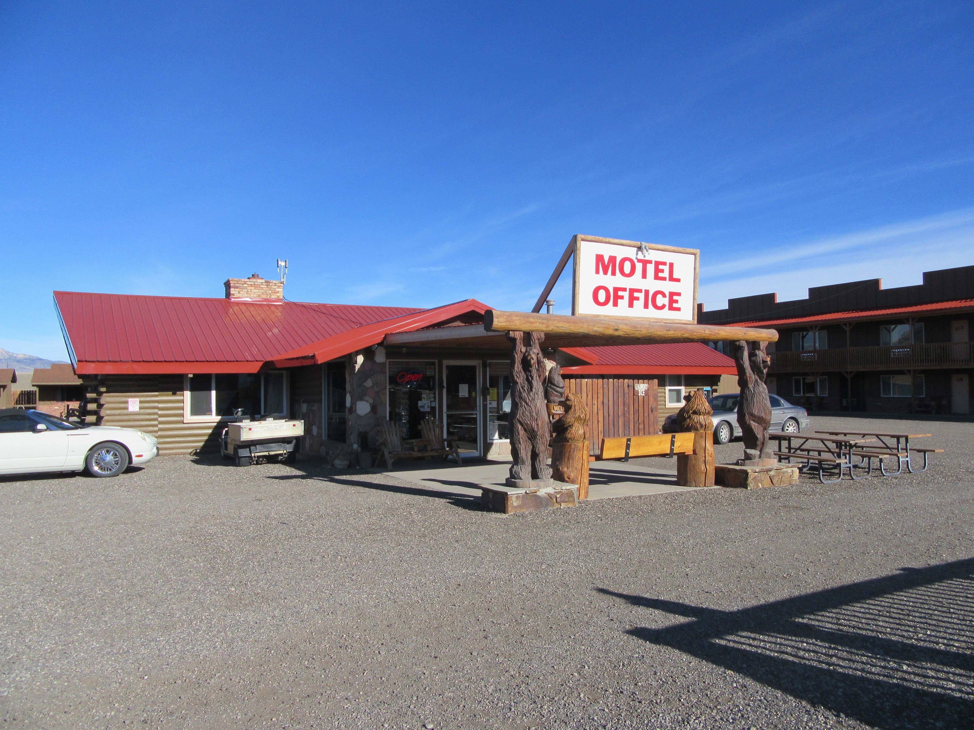 Oficina de motel con techo rojo, un cartel y una estructura de madera con bancos.