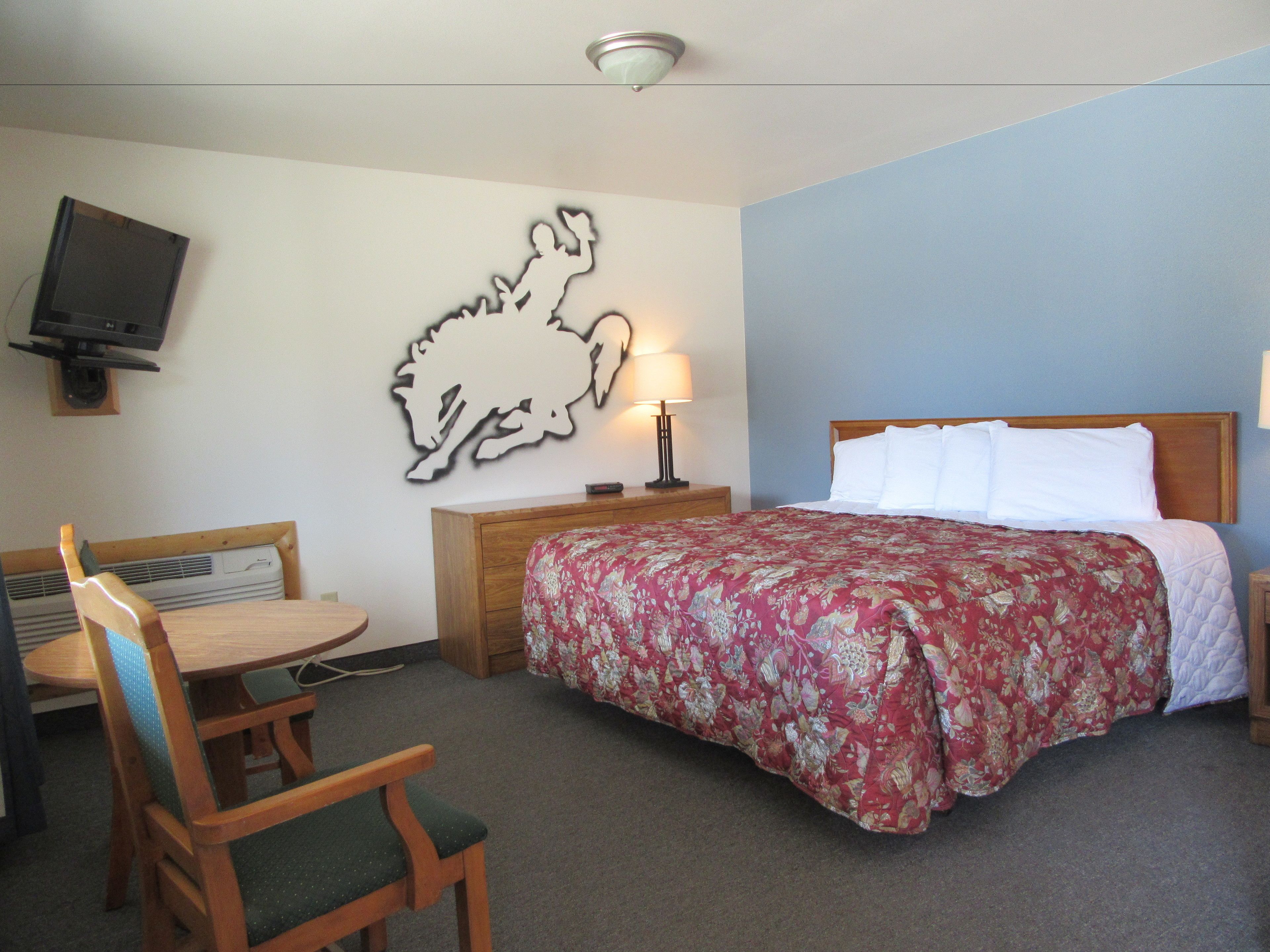 Hotelkamer met een bed, bureau, stoel, tv aan de muur en een wandlamp.