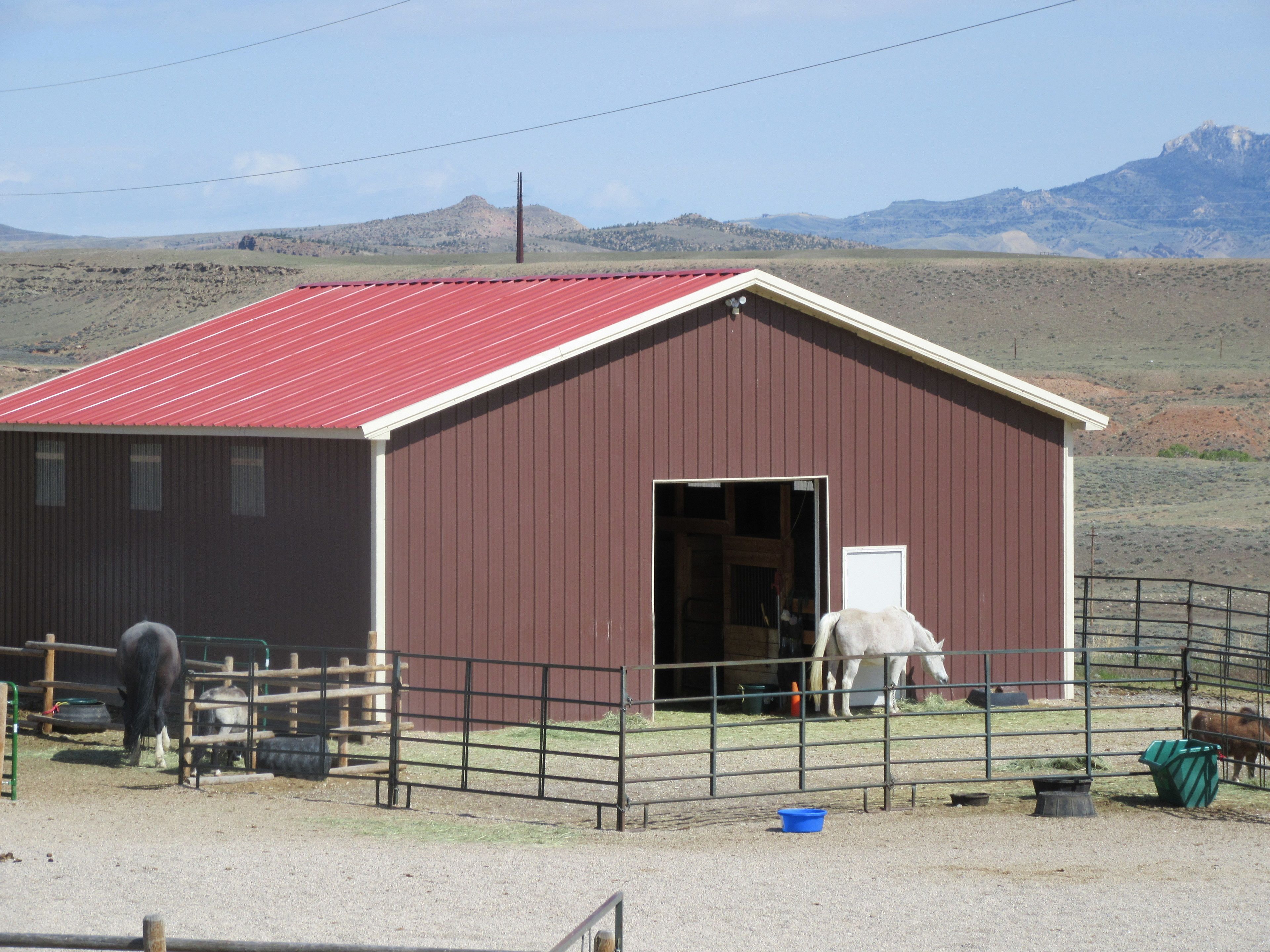 A red barn with a metal roof, a fenced area, and a horse visible inside.