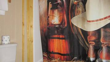 A bathroom with a white toilet, a shower curtain depicting a lantern and cowboy hat, and a towel rack.