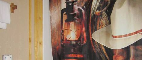 A bathroom with a white toilet, a shower curtain depicting a lantern and cowboy hat, and a towel rack.
