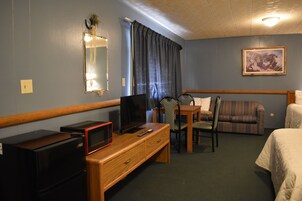 Habitación de hotel con escritorio de madera, televisión, microondas, silla, sofá y cama.