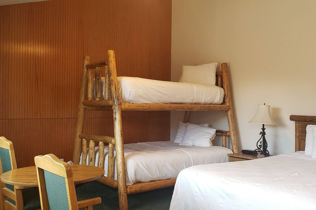 A bunk bed room with a wooden headboard, two single beds, a desk with a chair, and a lamp.