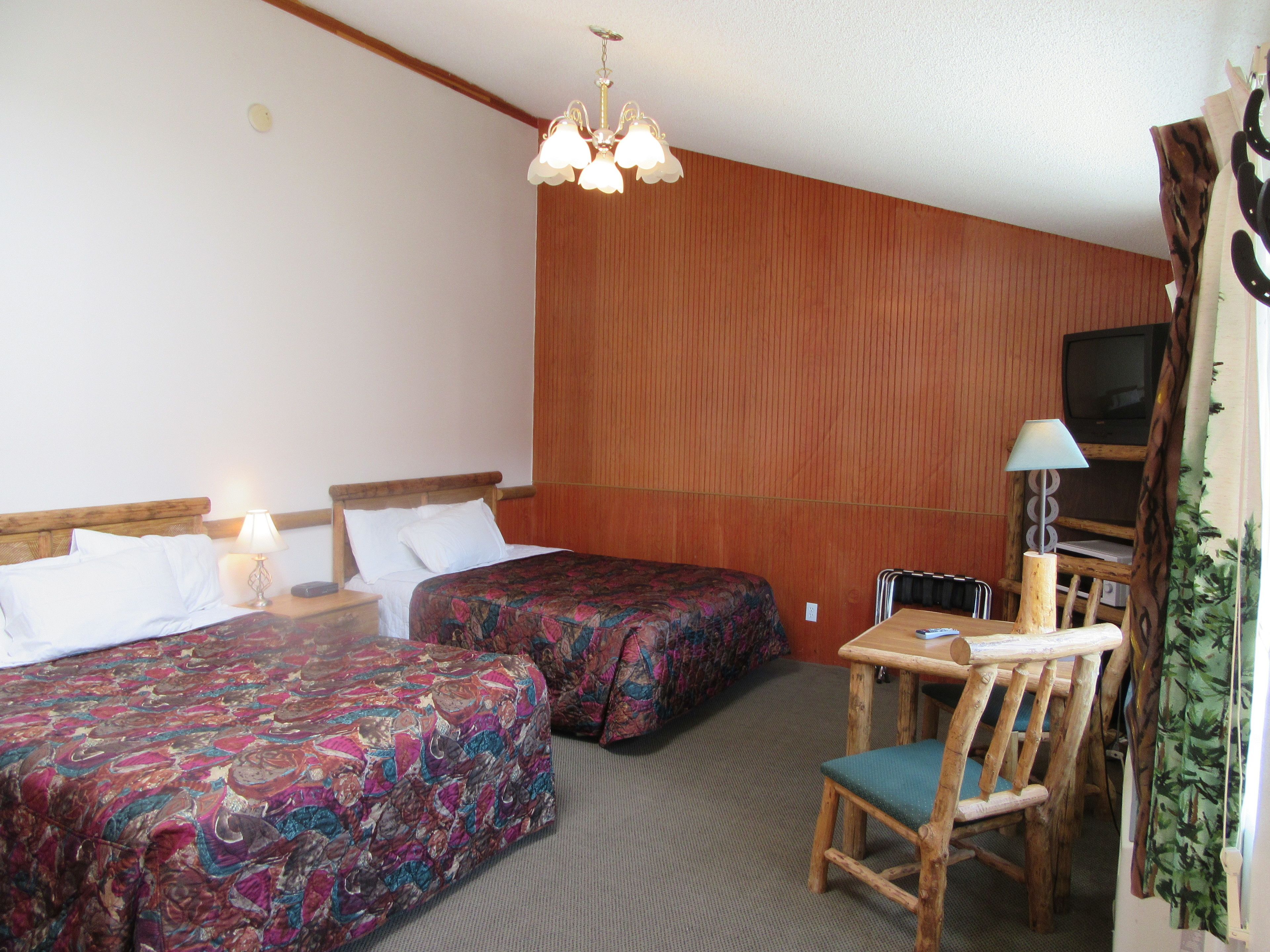 Een hotelkamer met twee bedden, een bureau met stoel, een televisie en een kroonluchter.