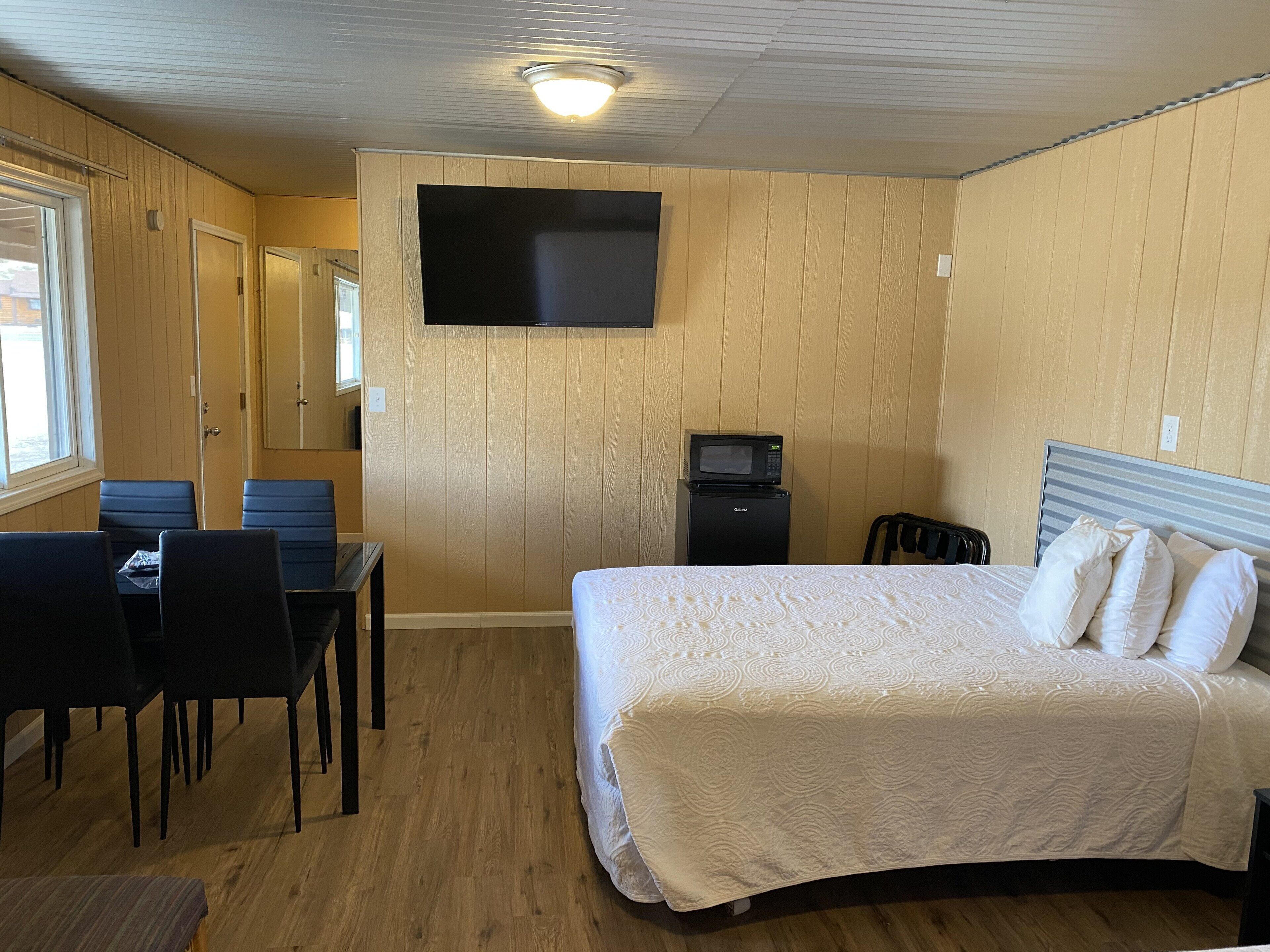 A hotel room with a bed, a desk with chairs, a flat-screen TV mounted on the wall, and a microwave.