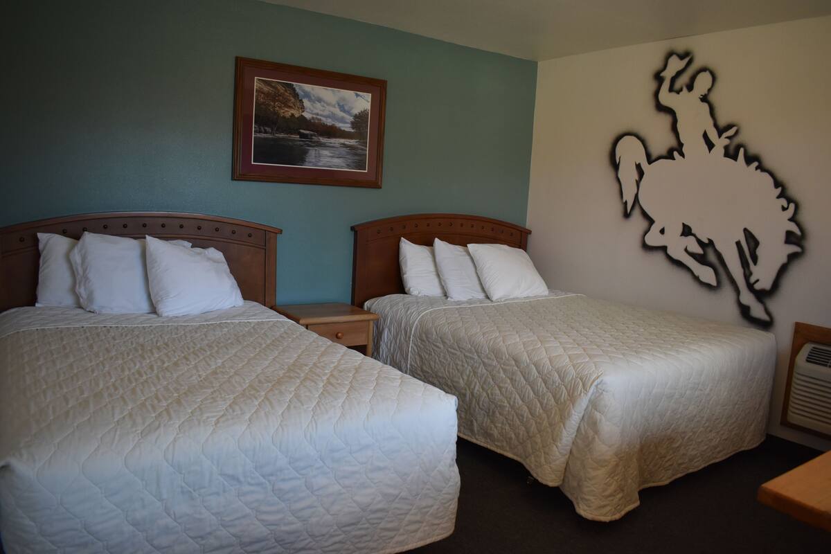 Two queen beds with white bedding, a framed picture on the wall, and a wall-mounted animal silhouette.