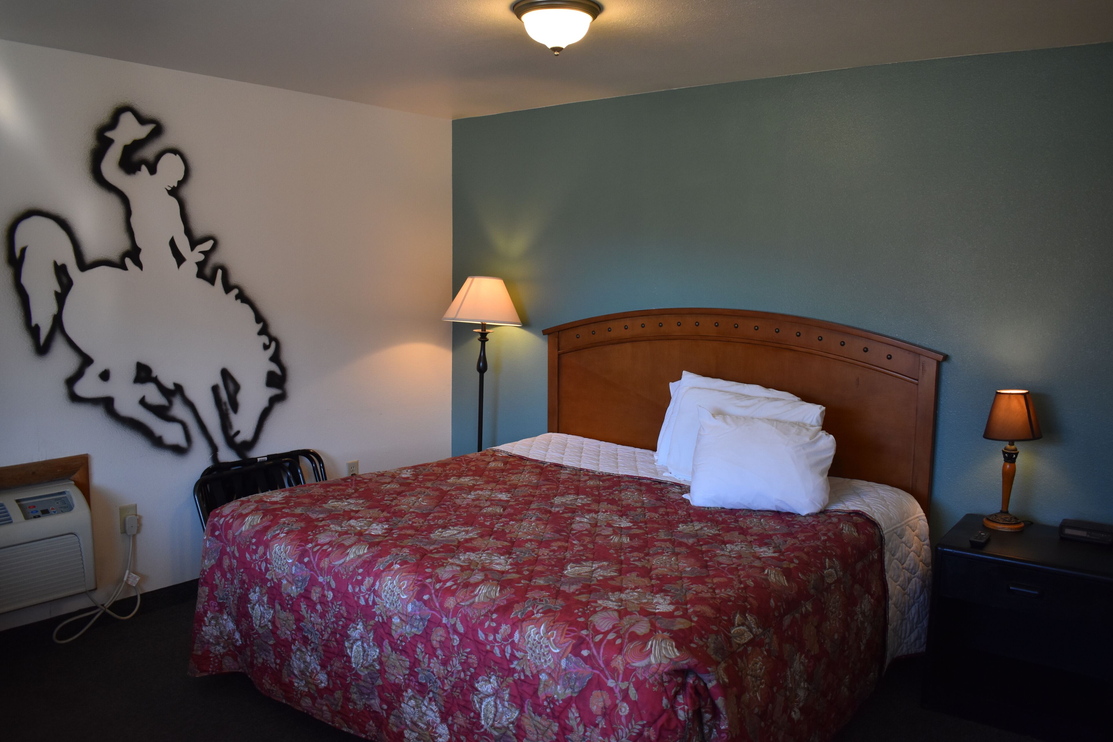 Habitación de hotel con cama, mesita de noche, lámpara, decoración en la pared y termostato.