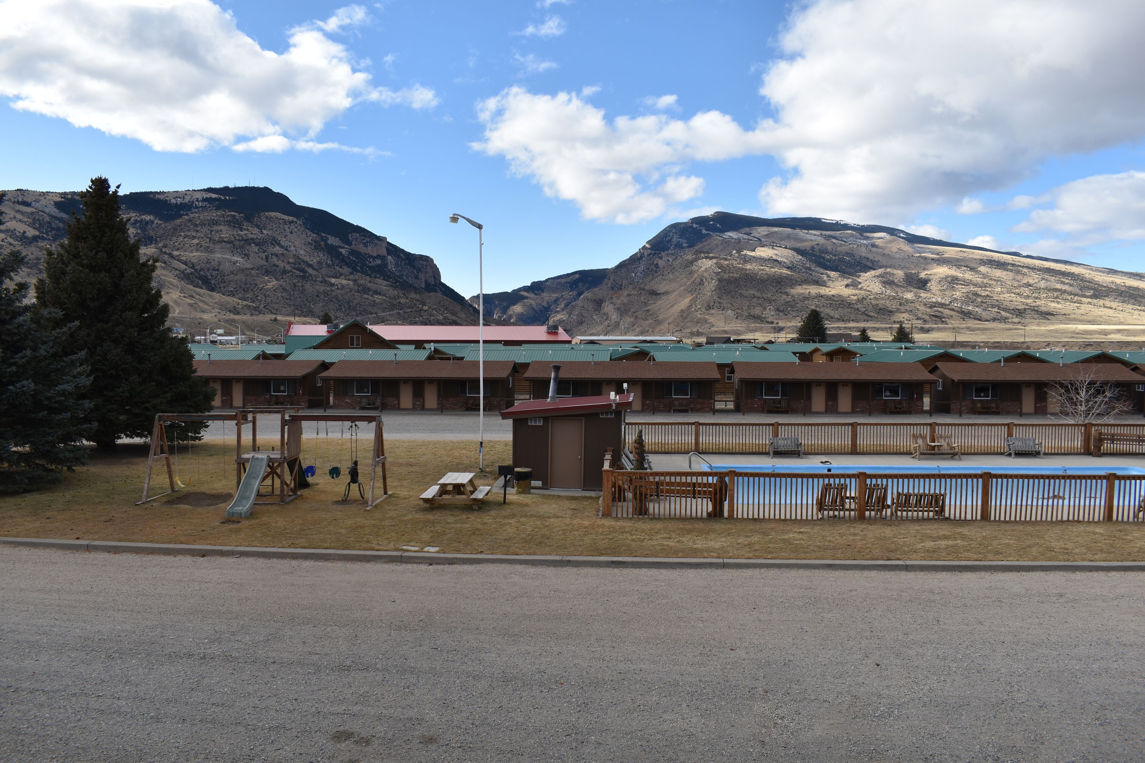 A motel with a playground, a pool, and mountains in the background.