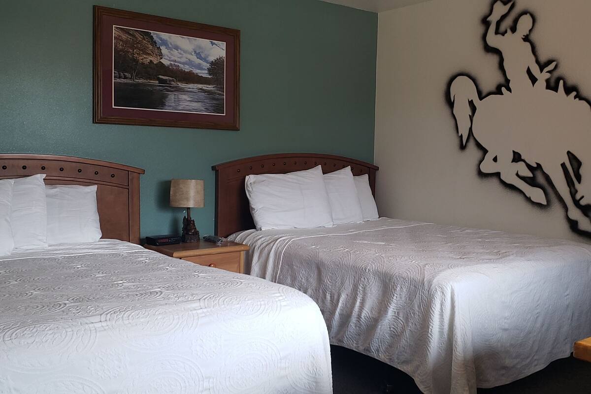A hotel room with two beds, a nightstand with a lamp, a framed picture on the wall, and a decorative wall piece.