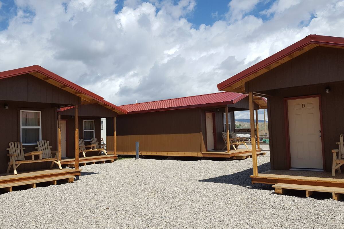 A row of wooden cabins with red roofs, each featuring a porch with wooden chairs.