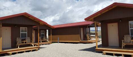 A row of wooden cabins with red roofs, each featuring a porch with wooden chairs.