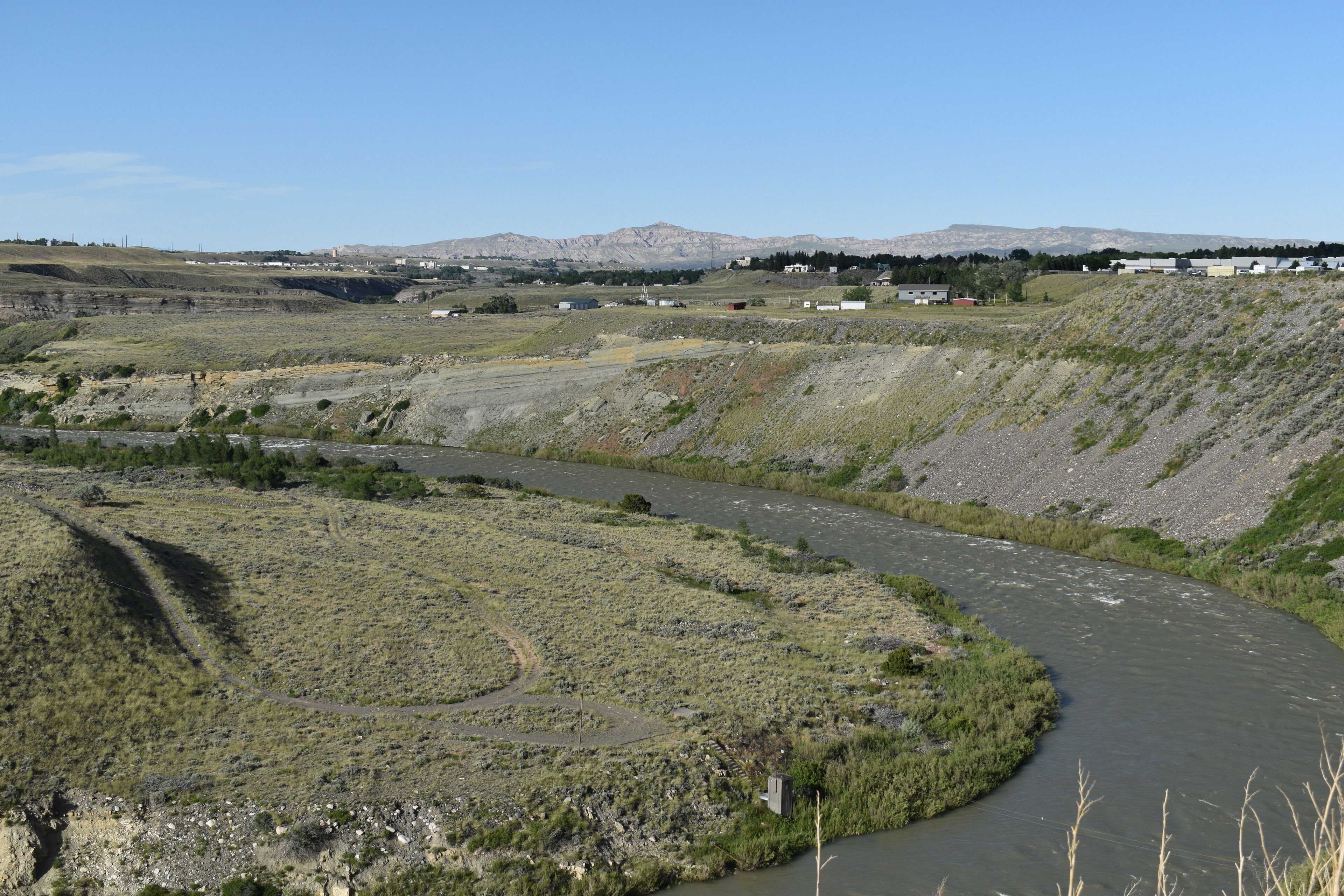 Un río serpentea por un paisaje montañoso con vegetación escasa y algunos edificios a lo lejos.