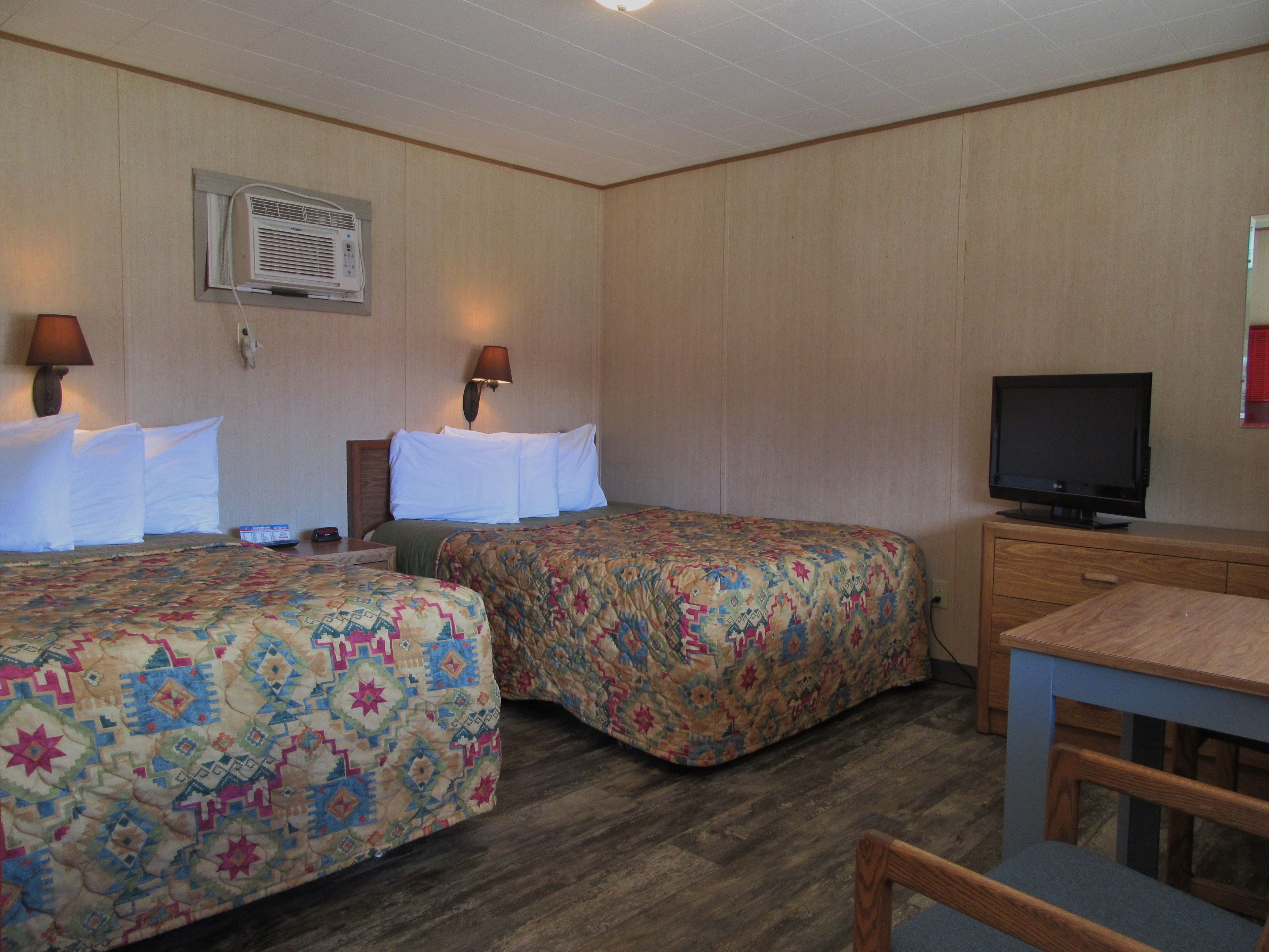 Quarto de hotel com duas camas, televisão, escrivaninha e abajur.