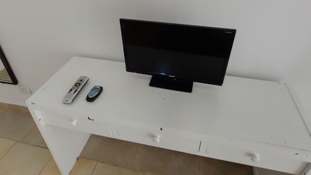 A white TV stand with a flat-screen TV, two remote controls, and a power strip. - Gran Hotel Casablanca (Villa Carlos Paz)