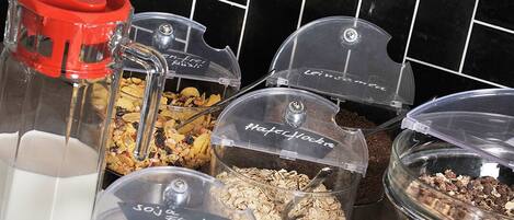A breakfast buffet with various food items in clear containers, including cereals, nuts, and dried fruits.