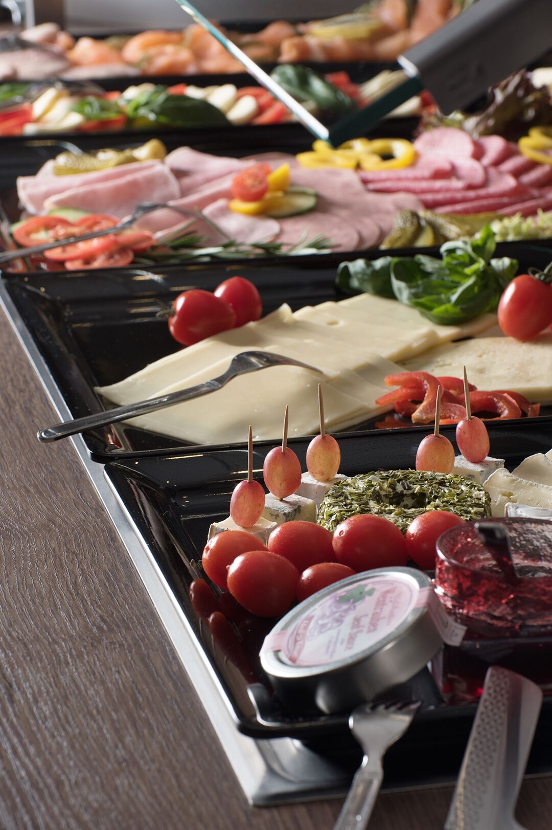 Un bufé con diversas opciones de comida, incluyendo quesos, carnes y vegetales.
