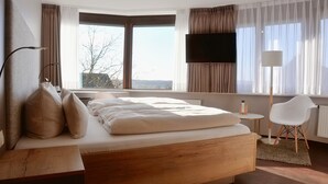 Habitación de hotel moderna con una cama grande, un escritorio, una silla, un televisor y una ventana con cortinas.