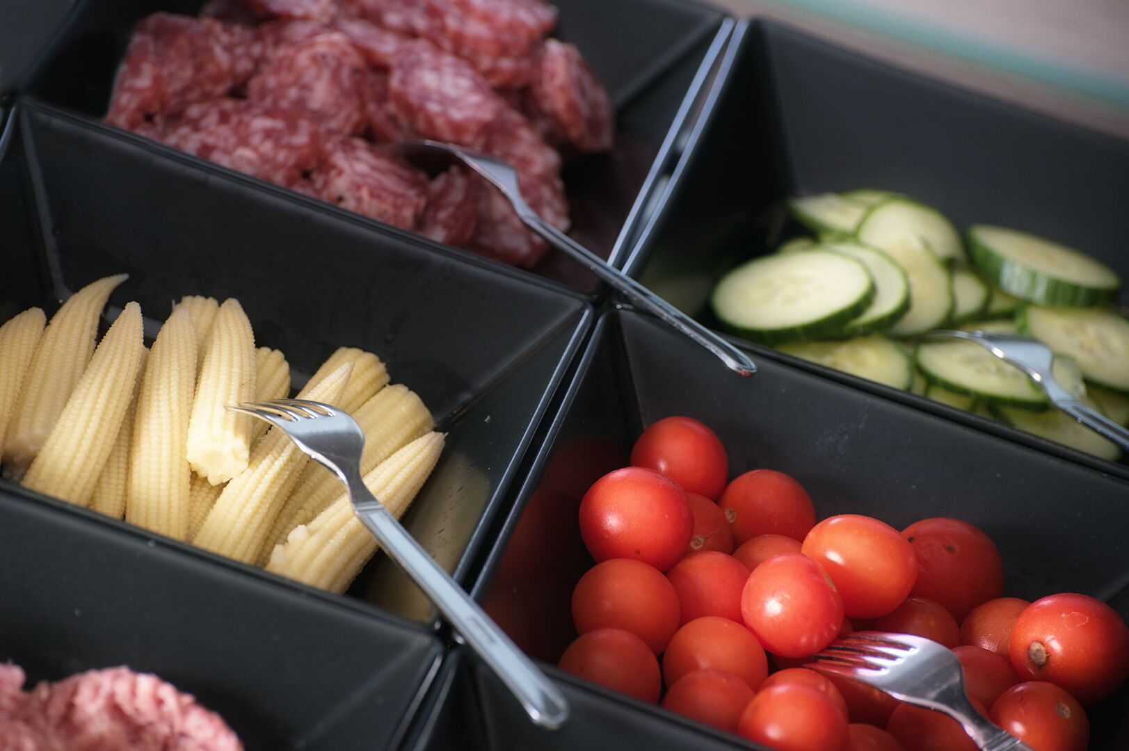 A food display with pasta, tomatoes, and sliced cucumbers.