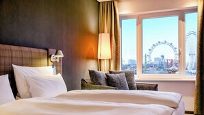 A hotel room with a large bed, a headboard, a lamp, a chair, and a window with a view of a Ferris wheel. - Motel One Wien-Prater (Vienna)