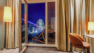 Ein Hotelzimmer mit Blick auf ein Riesenrad bei Nacht, ein Sessel, ein Tisch und Vorhänge.