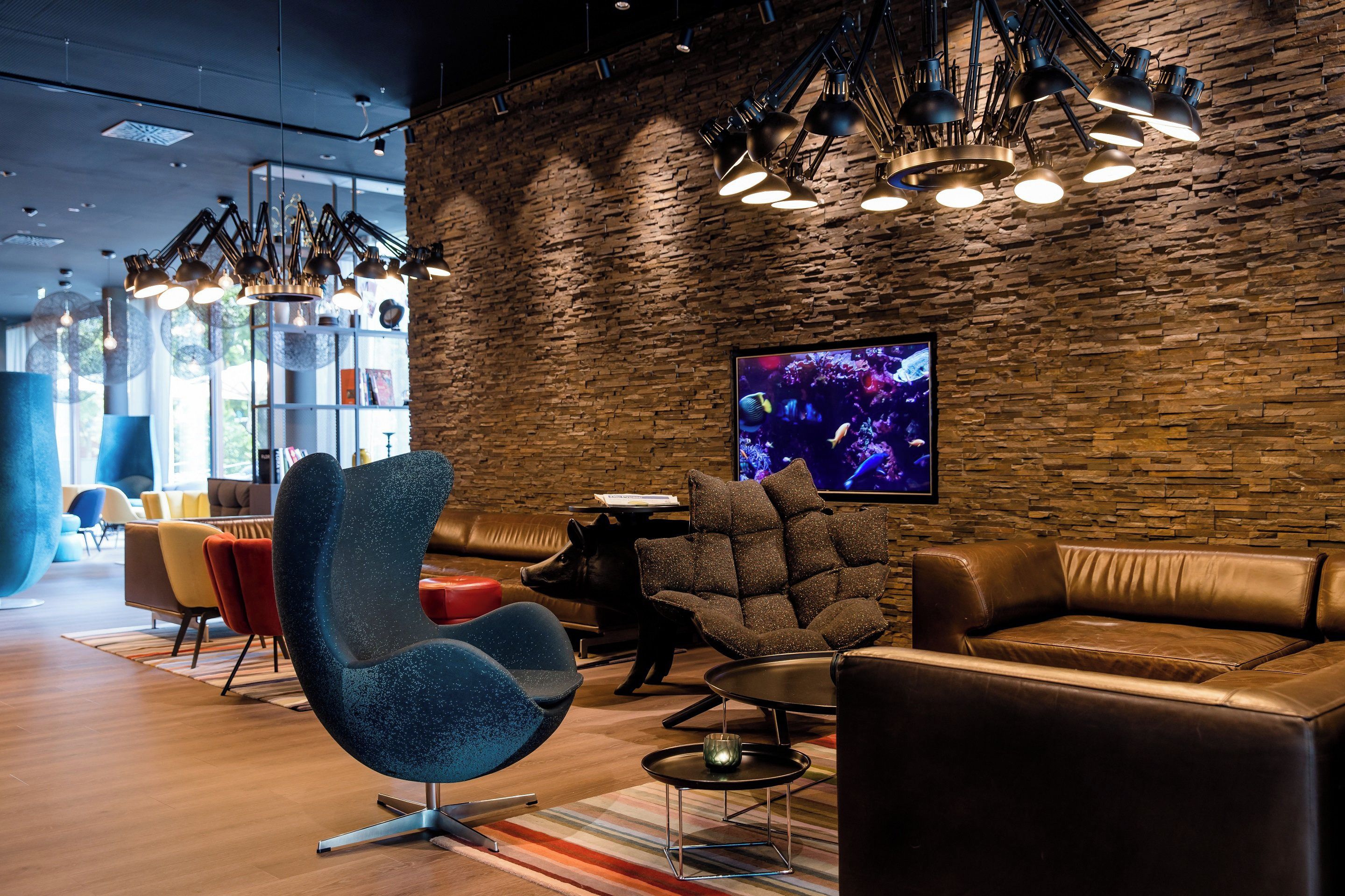 A modern lounge area with leather sofas, a unique blue chair, and a stone wall.