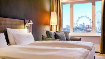 A hotel room with a large bed, a headboard, a lamp, a chair, and a window with a view of a Ferris wheel.