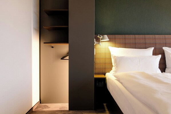 Una habitación de hotel con cama, mesita de noche, lámpara y estante en la pared.