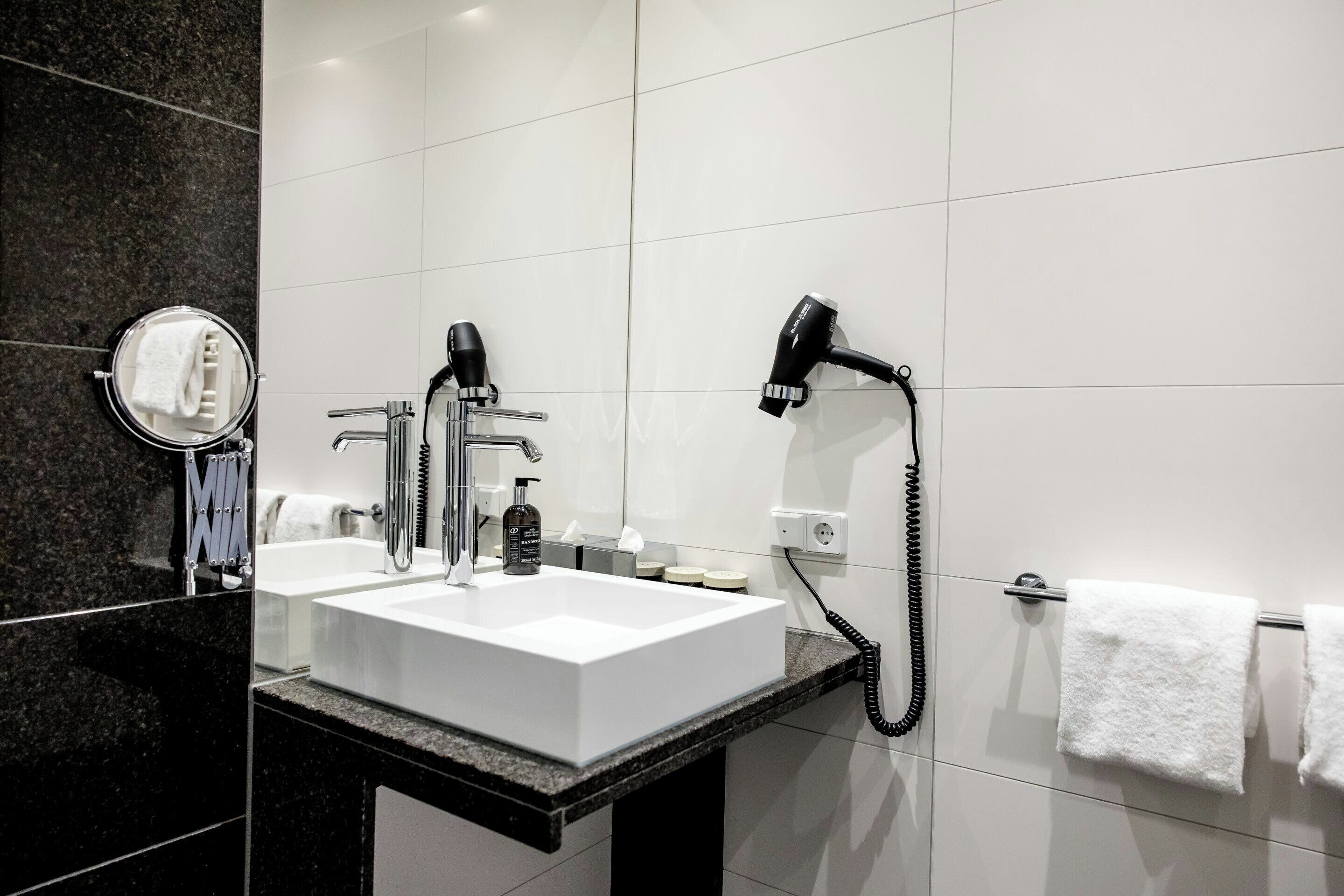 A modern bathroom with a white sink, two faucets, a hairdryer, and a towel rack.